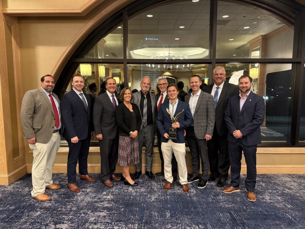 Clay County Team and Scorpio Team stand together holding the ABC Eagle Award in a banquet room