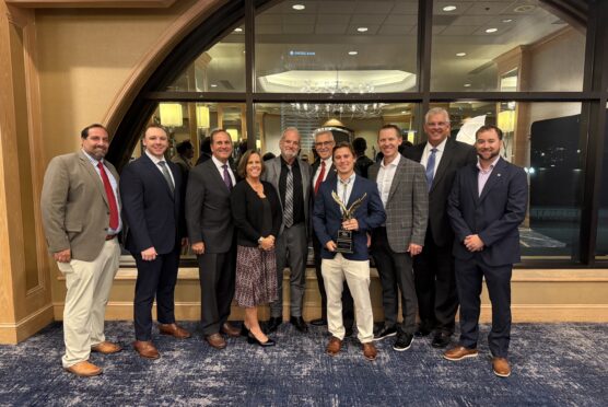 Clay County Team and Scorpio Team stand together holding the ABC Eagle Award in a banquet room