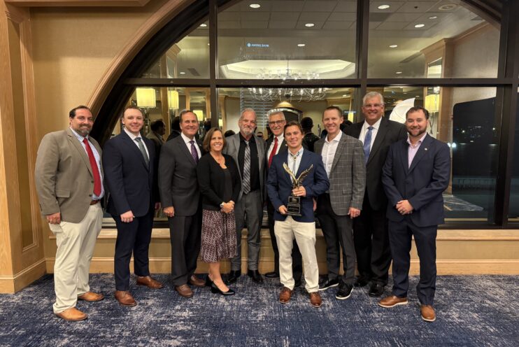 Clay County Team and Scorpio Team stand together holding the ABC Eagle Award in a banquet room